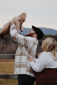 a family is holding a baby in the air in front of a fence