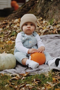 a baby in overalls sitting on a blanket with pumpkins