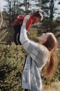 a woman holding a child in a christmas tree field