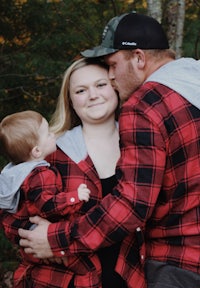 a man and woman hugging a baby in a red flannel shirt