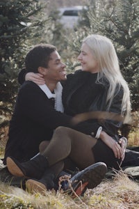 a couple sits on the ground in front of a christmas tree farm