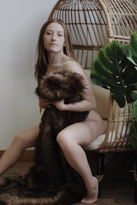 a woman sitting in a wicker chair with a furry blanket