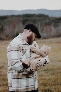 a man holding a baby in a field with mountains in the background