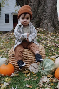 a baby sitting on a wicker basket in front of pumpkins