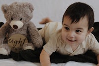 a baby laying on a bed with a teddy bear