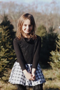 a little girl standing in front of a christmas tree farm