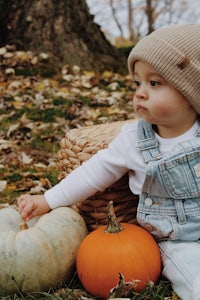 a baby in overalls sitting next to a pumpkin