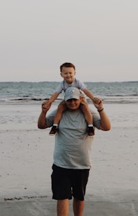 a man holding a child on his shoulders on the beach