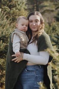 a woman holding a baby in front of a christmas tree farm