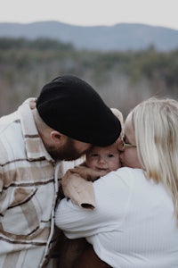 a man and woman hugging a baby in a field