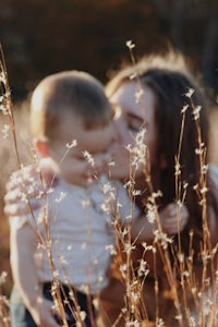 a woman kissing her child in a field of tall grass