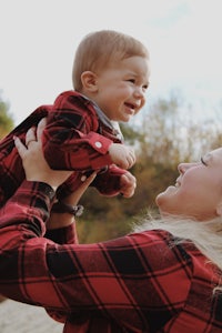 a woman in a red plaid shirt is holding a baby in her arms