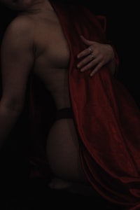 a naked woman posing under a red cloth