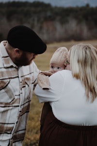 a man and woman hugging a baby in a field