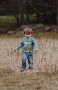 a young boy is running through a field with a frisbee