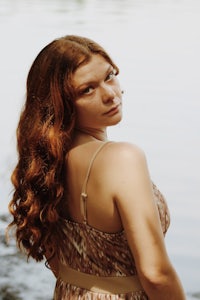 a woman in a brown dress standing next to a body of water