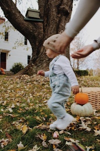 a baby is running in front of a pumpkin patch