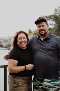 a man and woman posing for a photo in front of a body of water