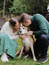 a man and woman kissing a dog in the grass