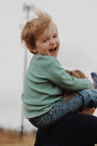 a woman is holding a child on her shoulders in a field