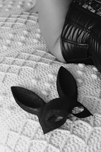 black and white photo of a woman laying on a bed with a bunny mask