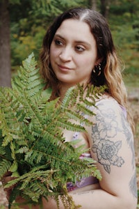 a woman with tattoos holding a bunch of ferns